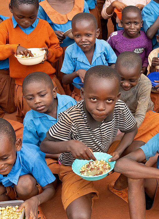 Eine warme Mahlzeit für die Schulkinder von Kilifi Eine Gruppe Kinder sitzt mit vollen tellern auf dem Boden