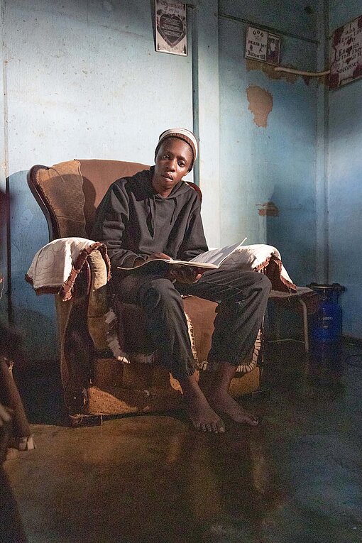 Eine junge Frau sitzt ernst in einem Sessel, der mit braunem Velours bezogen ist