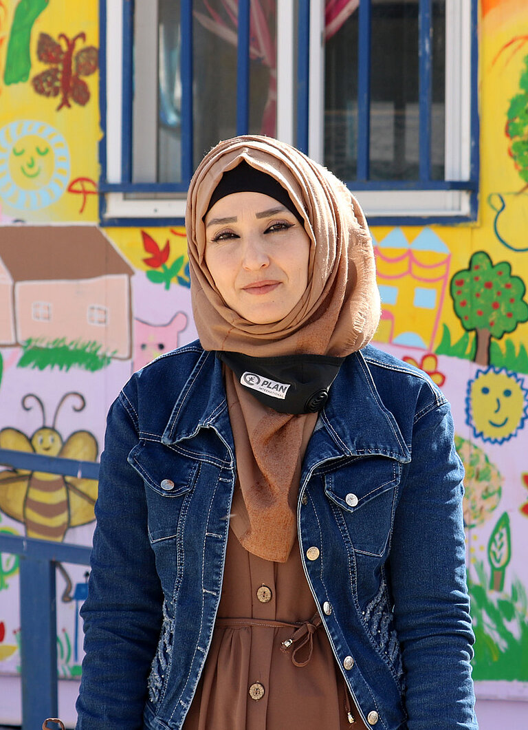 Alia, eine junge Frau, steht vor einem bunt bemalten Gebäude.