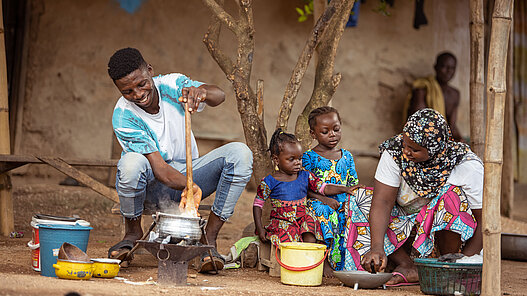 Ein junger Mann, zwei Kinder und eine Frau bereiten in Ghana gemeinsam Essen zu
