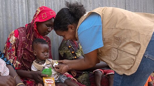 Plan International Mitarbeiterin untersucht kleinen Jungen auf Unterernährung
