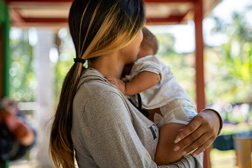 Eine Frau hält ein Baby im Arm, sie ist nur von der Seite zu sehen