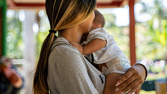 Eine Frau hält ein Baby im Arm, sie ist nur von der Seite zu sehen