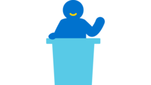 Icon von einer Person, die hinter einem Rednerpult steht und einen Vortrag hält.