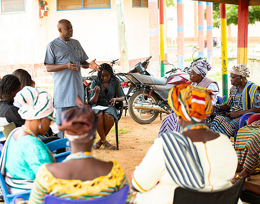Die Königinnenmütter sitzen bei einer Schulung draußen im Kreis in ihrer Gemeinde
