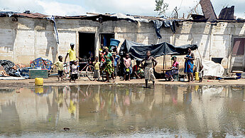 Einige Menschen stehen mit hoffnungslosem Gesichtsausdruck vor einem heruntergekommenden Haus, das von Wasser umgeben ist. Das Foto ist von Emidio Jozine in Mosambik aufgenommen worden, nachdem Zyklon Idai schwere Schäden angerichtet hatte.