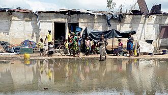 Einige Menschen stehen mit hoffnungslosem Gesichtsausdruck vor einem heruntergekommenden Haus, das von Wasser umgeben ist. Das Foto ist von Emidio Jozine in Mosambik aufgenommen worden, nachdem Zyklon Idai schwere Schäden angerichtet hatte.
