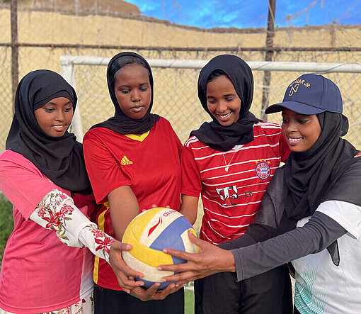 Vier junge Frauen halten gemeinsam einen Ball in die Kamera