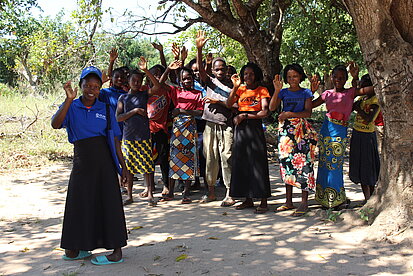 Eine Gruppe Jugendlicher steht unter einigen Bäumen und winkt