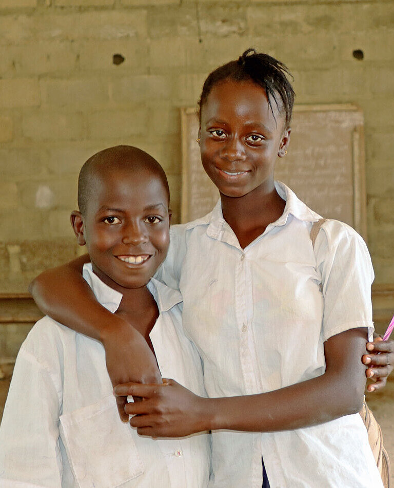 In einem kahlen Raum stehen ein Mädchen und ein Junge vor einer improvisierten Schultafel