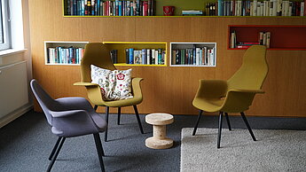 Heller Raum mit modernen Stühlen und Bücherwand, der eine gemütliche Gesprächsatmosphäre vermittelt.