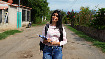 Teenagerin trägt Schulrucksack und Notizblock, unterwegs in einer ländlichen Gegend. Bildung als Schlüssel für die Zukunft.