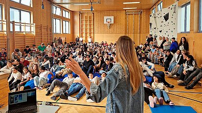 Lisa Buchner steht vor Schüler:innen in einer Sporthalle. Gebannt hören sie ihr bei ihrem Vortrag zu.
