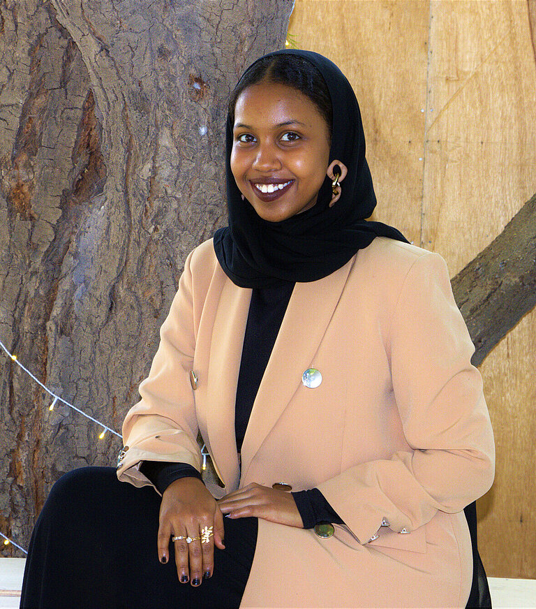 Eine junge Frau aus Somaliland sitzt vor einem Baum und lächelt in die Kamera.
