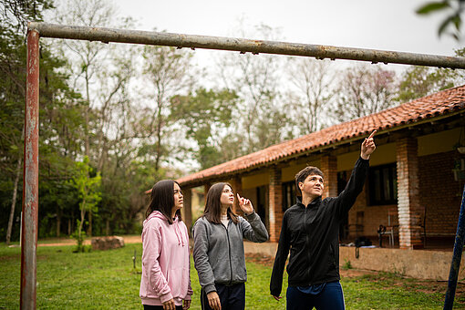 Ein jugendlicher Junge zeigt zwei jugendlichen Mädchen ein marodes Schaukelgerüst