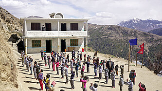 Auf einem Platz vor einem Schulgebäude im Himalaja-Gebirge stehen Schulkinder