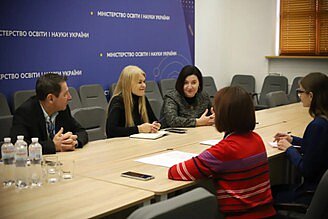 Vier Frauen und ein Mann sitzen an einem Tisch. Es sieht nach einem Business-Meeting aus.