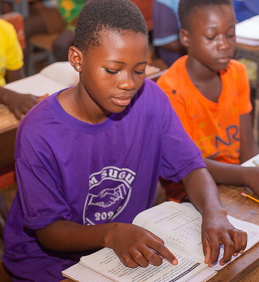 Eine ghanaische Teenagerin sitzt in der Schule und liest in einem Textbuch