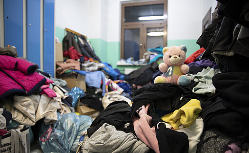 In einem Zimmer stapeln sich Sachspenden, unter anderem ein bunter Teddybär.