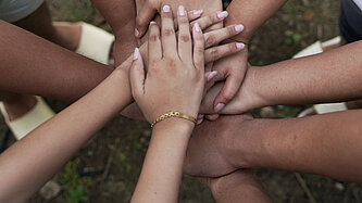 Mädchen stehen im Kreis und halten ihre Hände aufeinander.