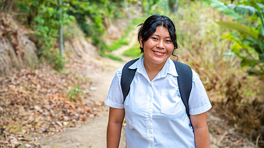 Junge Frau mit einem Rucksack auf dem Rücken ist im Grünen auf dem Weg zur Schule in El Salvador.