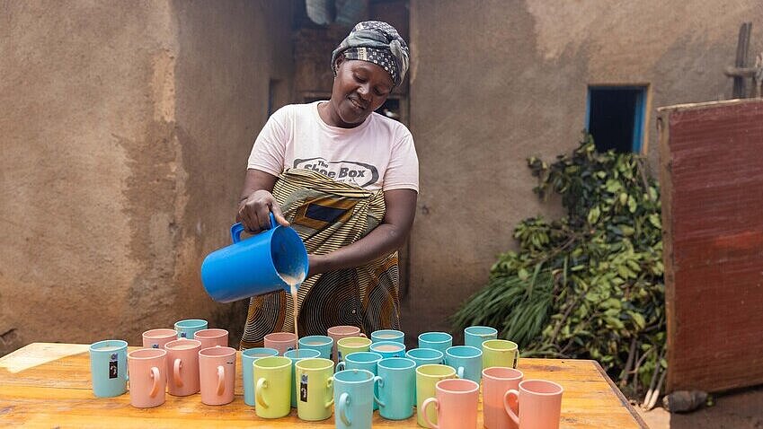 Eine Frau schenkt ein milchiges Getränk und bunte Becher ein