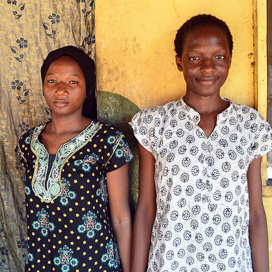 Fatouma und Koumba stehen vor einer Hauswand.