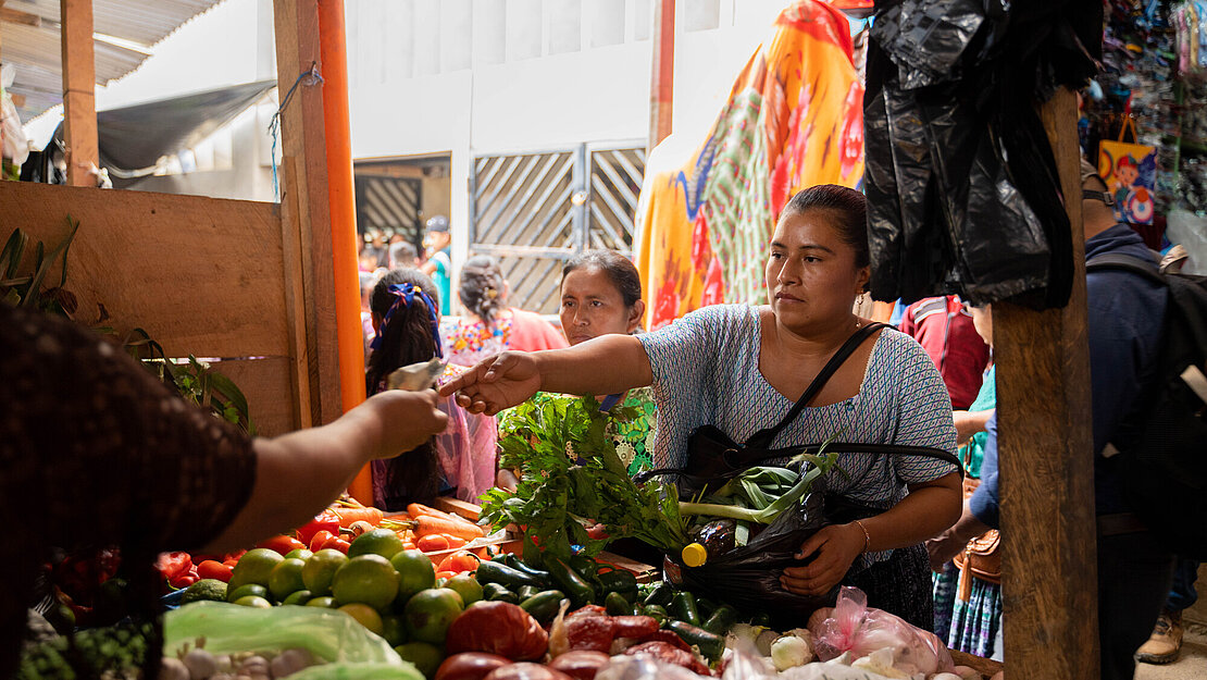 Eine Frau reicht Bargeld über einen Marktstand voller Gemüse