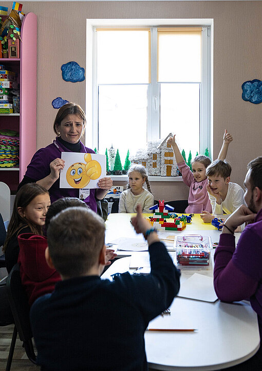 Eine Gruppe Kinder sitzt mit zwei Erwachsenen um einen Tisch.