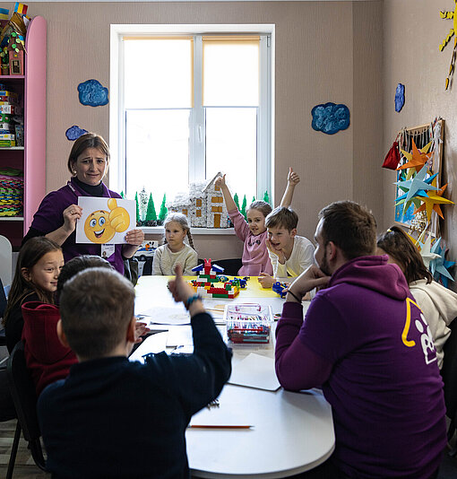 Eine Gruppe Kinder sitzt mit zwei Erwachsenen um einen Tisch.