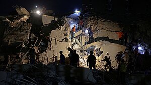 Dunkle Nachtaufnahme von Menschen, die in den Trümmern eines zerstörten Gebäudes nach Überlebenden suchen. 