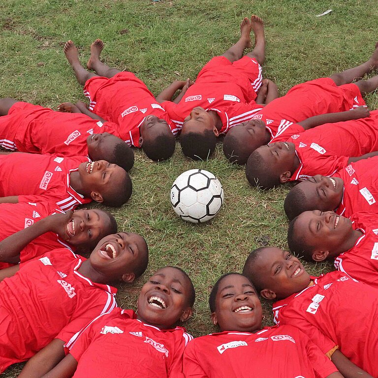 Kinder lachen und bilden auf dem Rasen einen Kreis um einen Fußball