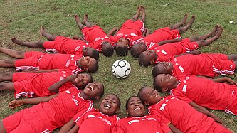 Kinder lachen und bilden auf dem Rasen einen Kreis um einen Fußball