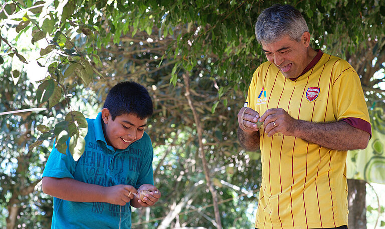 Ein Sohn und sein Vater stehen nebeneinander, halten Spielzeuge in den Händen und lachen.