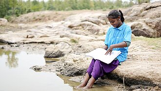 Mädchen sitzt am Wasser und lernt 
