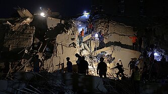 Nachtaufnahme eines eingestürzten Gebäudes, das beleuchtet wird und auf dem sich Rettungskräfte befinden
