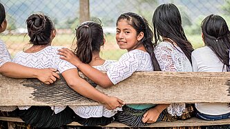 Eine Gruppe Mädchen sitzt auf einer Bank und eines von ihnen dreht sich über die Schulter um und schaut in die Kamera
