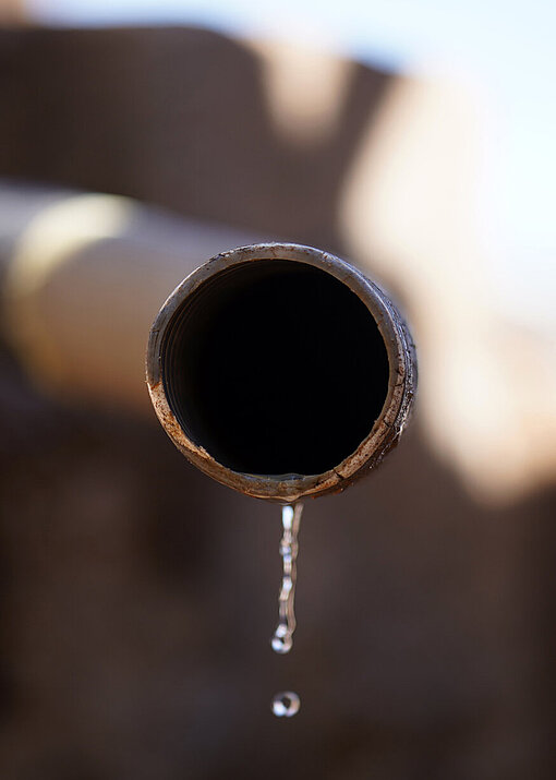 Aus einem Wasserrohr tropft ein dünnes Rinnsal Wasser.