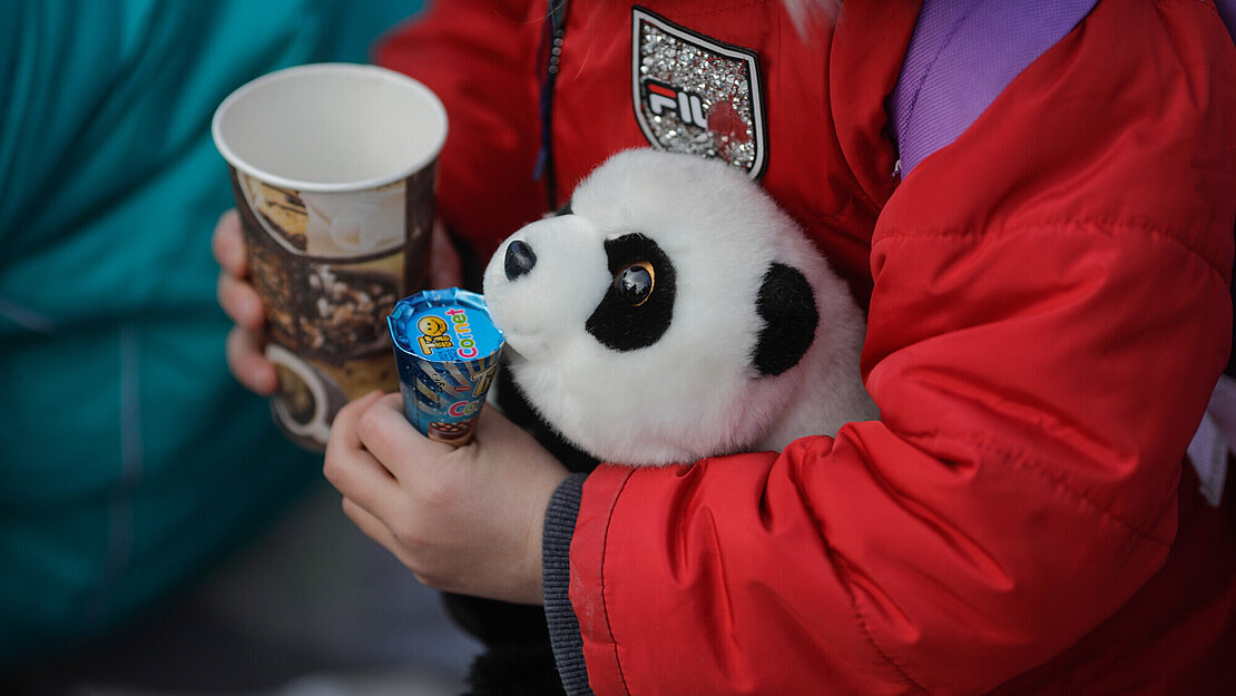 Ein Kind hält einen Stoff-Panda und einen Becher in der Hand