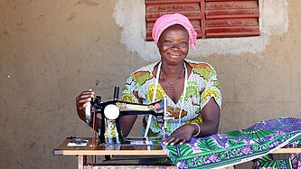 Eine Frau im bunten Kleid sitzt lachend an einer Nähmaschine