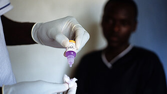 Eine Person mit Einmalhandschuhen tropft etwas aus einer kleinen Flasche in ein Stück Watte