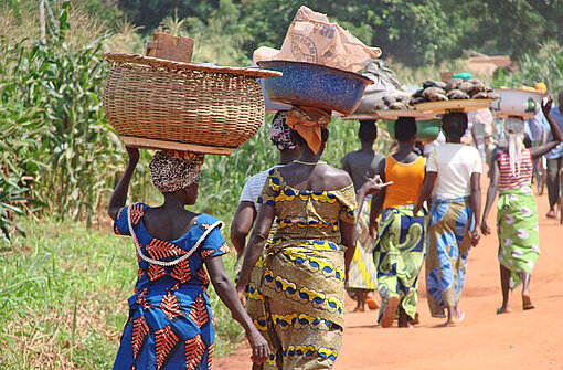 In Benin sind Frauen mit ihren Waren unterwegs zum örtlichen Markt Frauen in bunten Kleidern tragen Güter auf dem Kopf