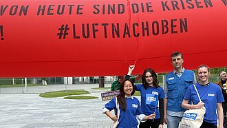 Vor einem roten Protestbanner stehen vier Mitarbeiter:innen von Plan International