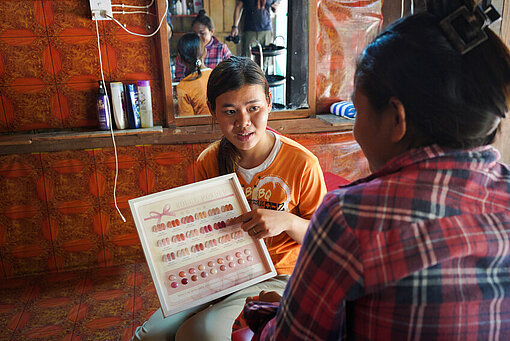 Eine Frau zeigt einer Kundin eine Farbpalette für Nagellack