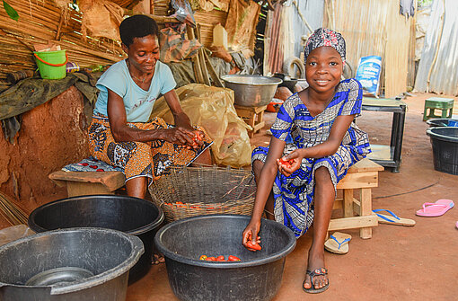 Anne und ihre Mutter sitzen vor einem Trog und sortieren Tomaten