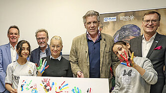 Mehrere Personen, darunter Kinder, stehen vor einem bunt gestalteten Plakat