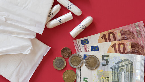Periodenarmut ist für fast ein Viertel der Menstruierenden ein Problem Binden, Tampons, Geldscheine und Münzen vor einem roten Hintergrund
