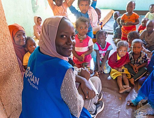 Eine Frau mit Logo von Plan International auf der Weste dreht sich lächelnd in die Kamera