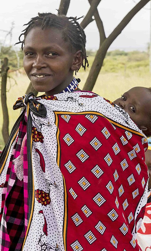 Eine afrikanische Frau in bunten Kleidern und mit einem Baby in einem Tuch auf den Rücken gebunden.