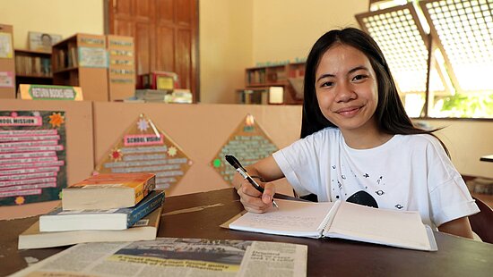 Bild: Ein junges Mädchen sitzt in der Schule und schreibt in ein Buch.
